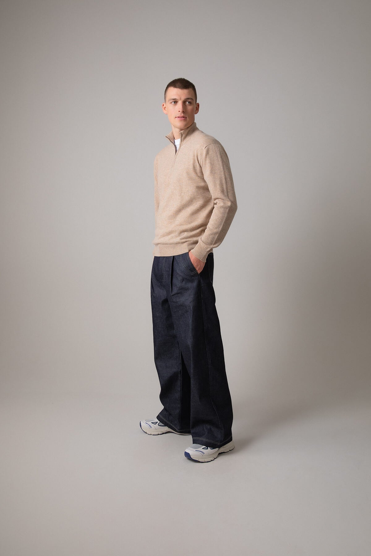 Johnstons of Elgin Men’s Cashmere Zip Neck Jumper in Oatmeal on model wearing navy trousers on grey background KAI05151HB0210