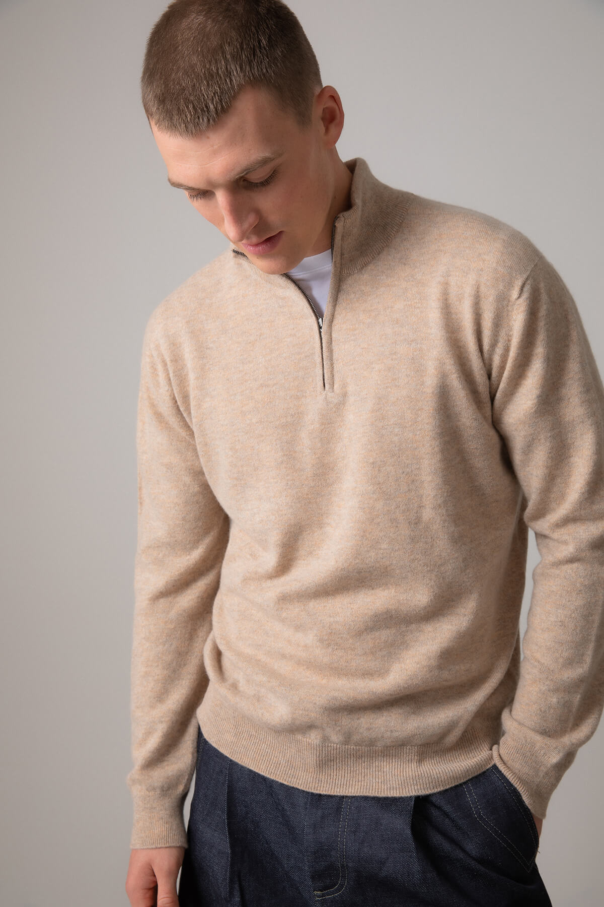 Johnstons of Elgin Men’s Cashmere Zip Neck Jumper in Oatmeal on model wearing navy trousers on grey background KAI05151HB0210