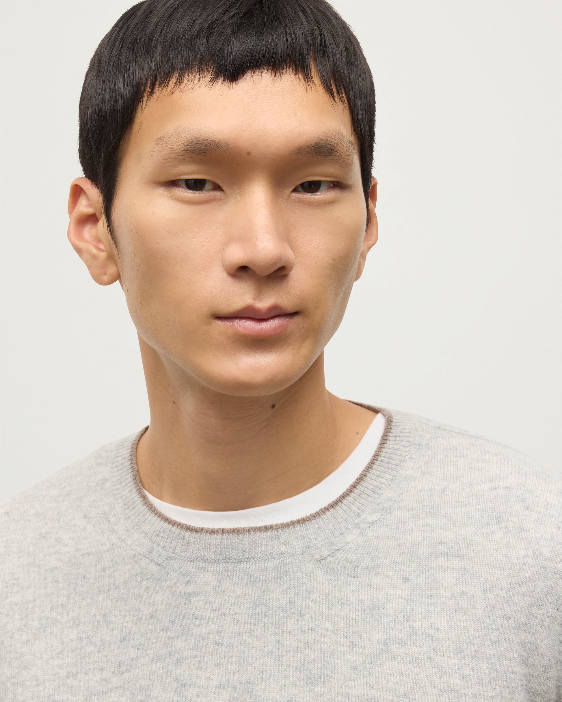 MODEL WEARING JOHNSTONS OF ELGIN MENS SHADED CREW SWEATER LIGHT GREY 100% CASHMERE OVER A WHITE T-SHIRT WITH GREY TROUSERS KAI05232Q25946