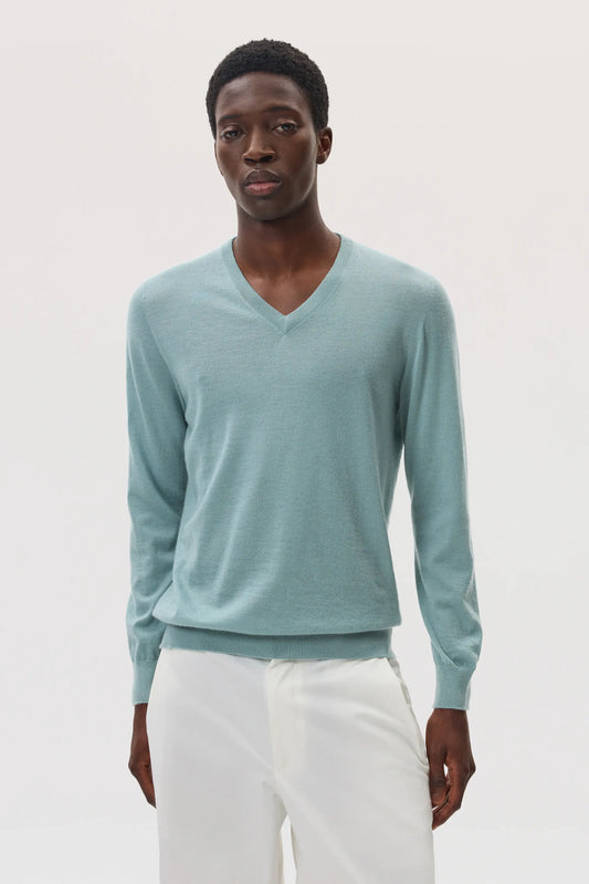 Male model wearing Johnstons of Elgin SS25 Unisex Knitwear Sage Superfine Cashmere V Neck Sweater with white trousers KAI05242SC0249