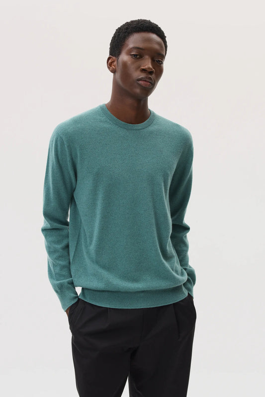 Model wearing Johnstons of Elgin SS25 Men's Knitwear Sage Classic Cashmere Round Neck Jumper with black trousers KAI05265SC4336