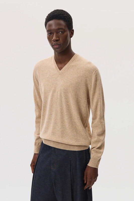 Model wearing Johnstons of Elgin SS25 Men's Knitwear Oatmeal Classic Cashmere V Neck Jumper with blue trousers  KAI05266HB0210