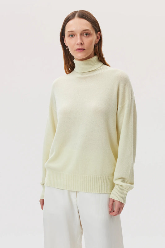 Model wearing Johnstons of Elgin SS25 Women's Knitwear Lemon Gauzy Cashmere Roll Neck with white trousers  KAI05324SA0145