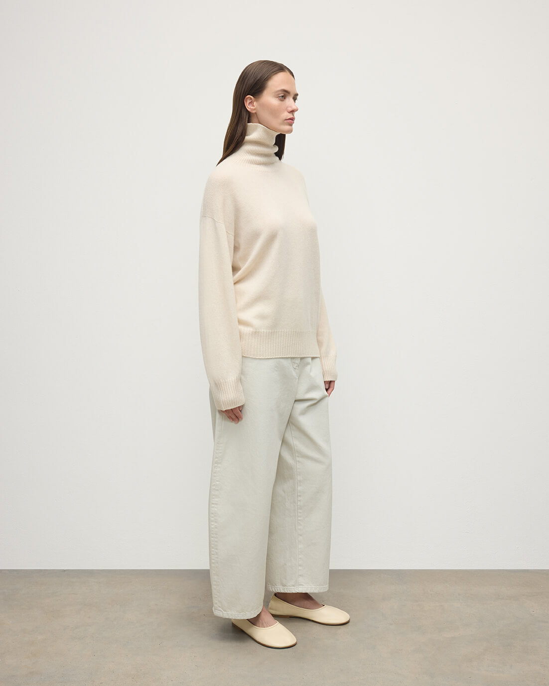 Model wears Johnstons of Elgin AW25 Women's Knitwear Champagne Gauzy Cashmere Cream Roll Neck Jumper Side View KAI05324SA0502