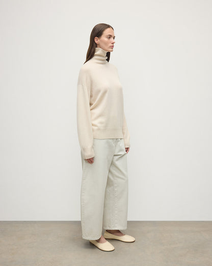 Model wears Johnstons of Elgin AW25 Women's Knitwear Champagne Gauzy Cashmere Cream Roll Neck Jumper Side View KAI05324SA0502