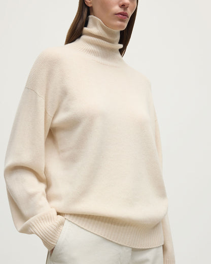 Model wears Johnstons of Elgin AW25 Women's Knitwear Champagne Gauzy Cashmere Cream Roll Neck Jumper Close Up  KAI05324SA0502