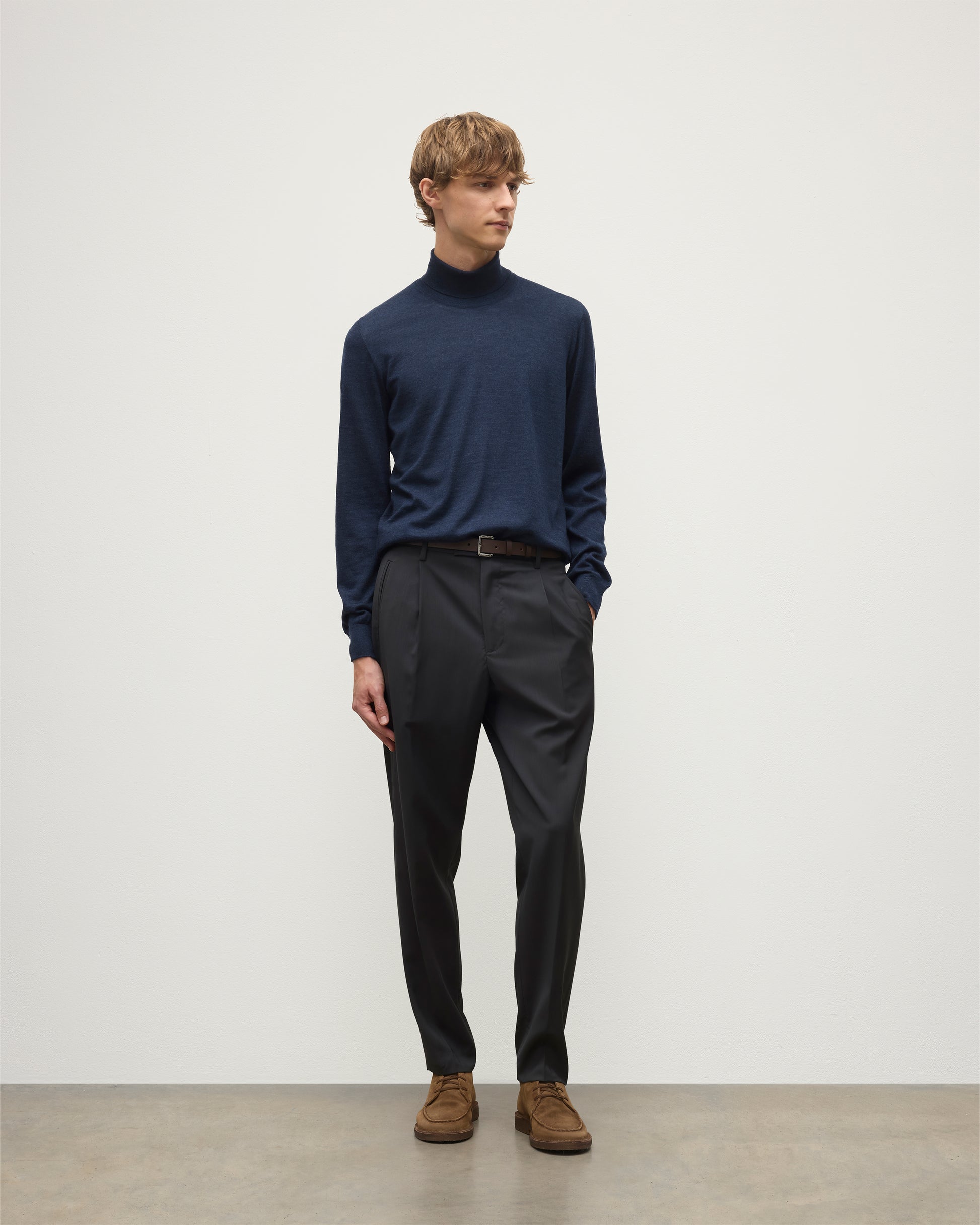 MODEL WEARS JOHNSTONS OF ELGIN MENS SUPERFINE FIN ROLL COLLAR NAVY 100% SUPERFINE CASHMERE  WITH GREY TROUSERS AND BROWN BELT KAI05333HD7350