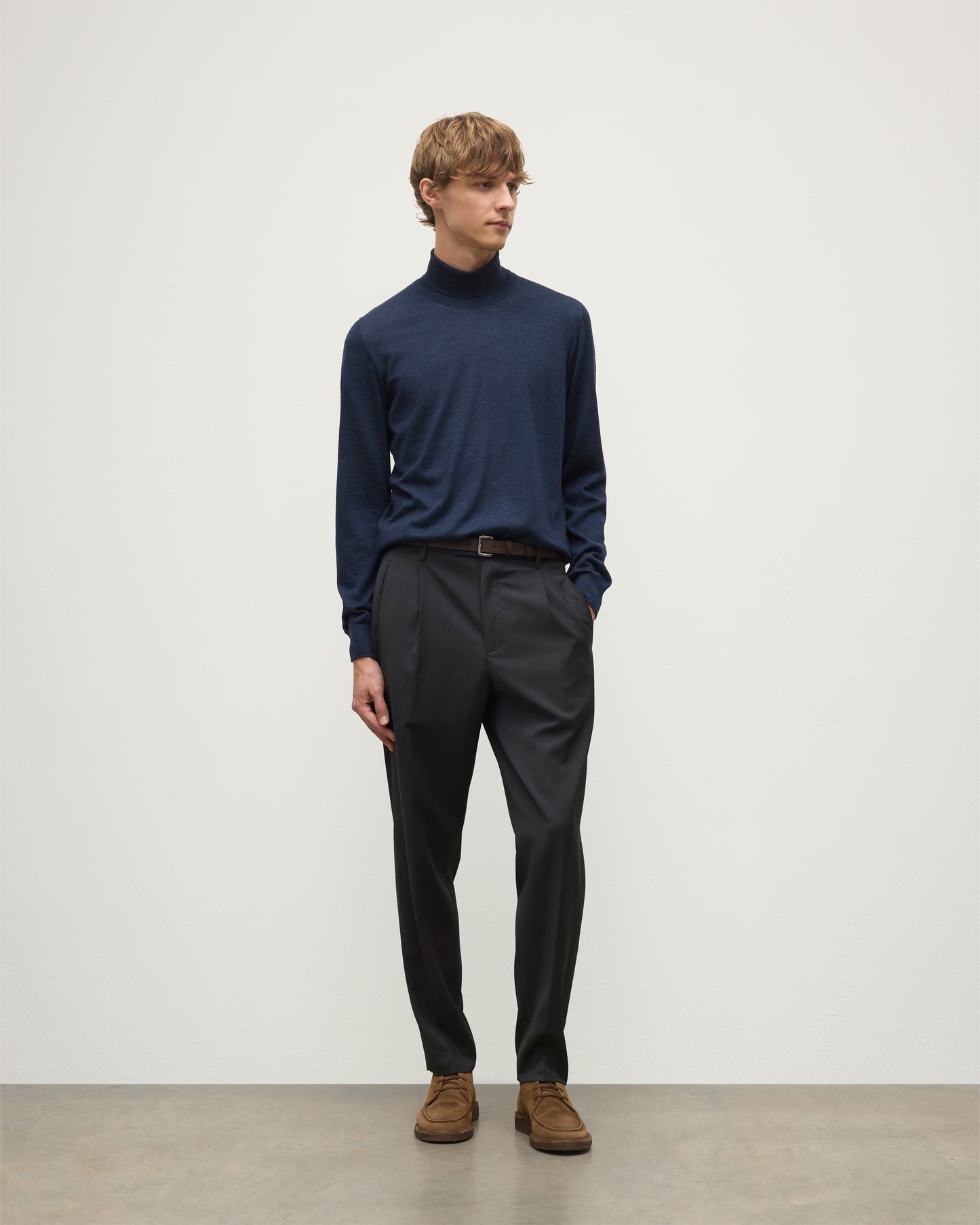 MODEL WEARS JOHNSTONS OF ELGIN MENS SUPERFINE FIN ROLL COLLAR NAVY 100% SUPERFINE CASHMERE  WITH GREY TROUSERS AND BROWN BELT KAI05333HD7350