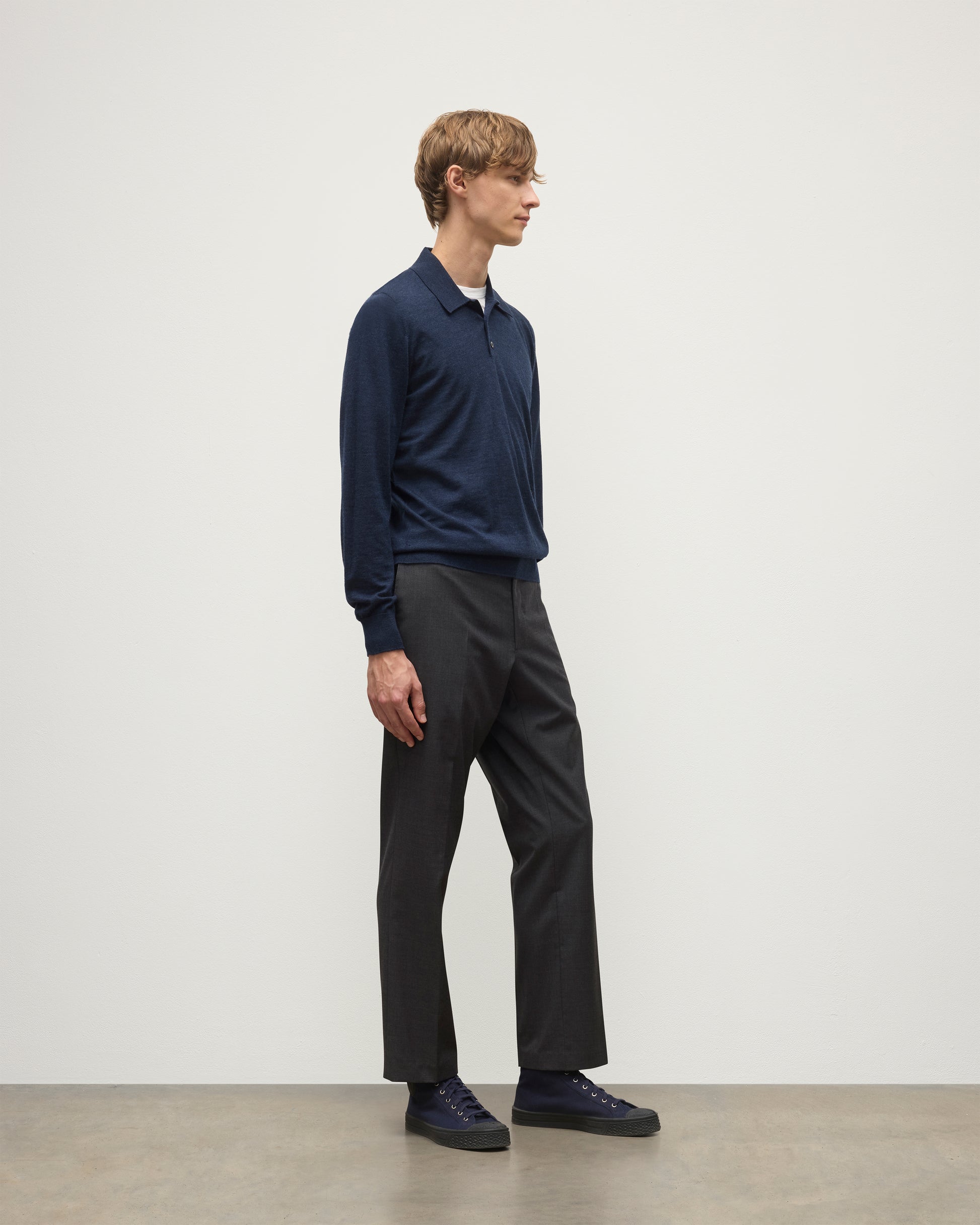 MODEL WEARS JOHNSTONS OF ELGIN MENS FIN SUPERFINE LONG SLEEVE POLOSHIRT NAVY 100% SUPERFINE CASHMERE OVER A WHITE T-SHIRT WITH GREY TROUSERS KAI05481HD7350