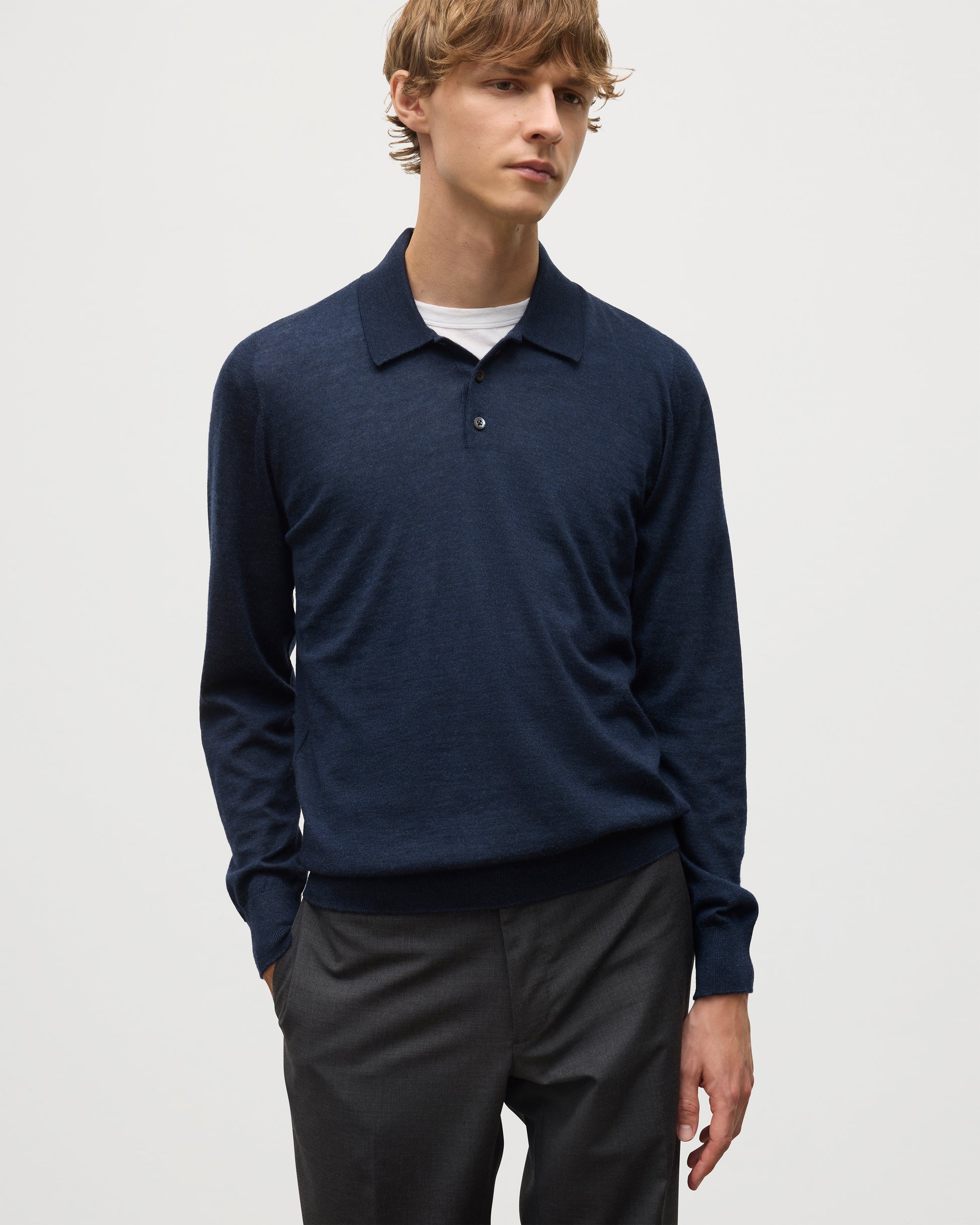 MODEL WEARS JOHNSTONS OF ELGIN MENS FIN SUPERFINE LONG SLEEVE POLOSHIRT NAVY 100% SUPERFINE CASHMERE OVER A WHITE T-SHIRT WITH GREY TROUSERS KAI05481HD7350