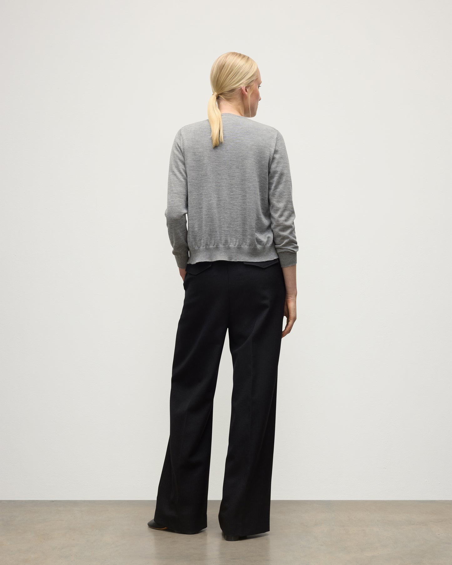 BACK OF A MODEL WEARING JOHNSTONS OF ELGIN WOMENS HONOR CREW CARDIGAN GREY 100% SUPERFINE CASHMERE OVER A MATCHING T-SHIRT WITH BLACK TROUSERS KAI05708HA4253