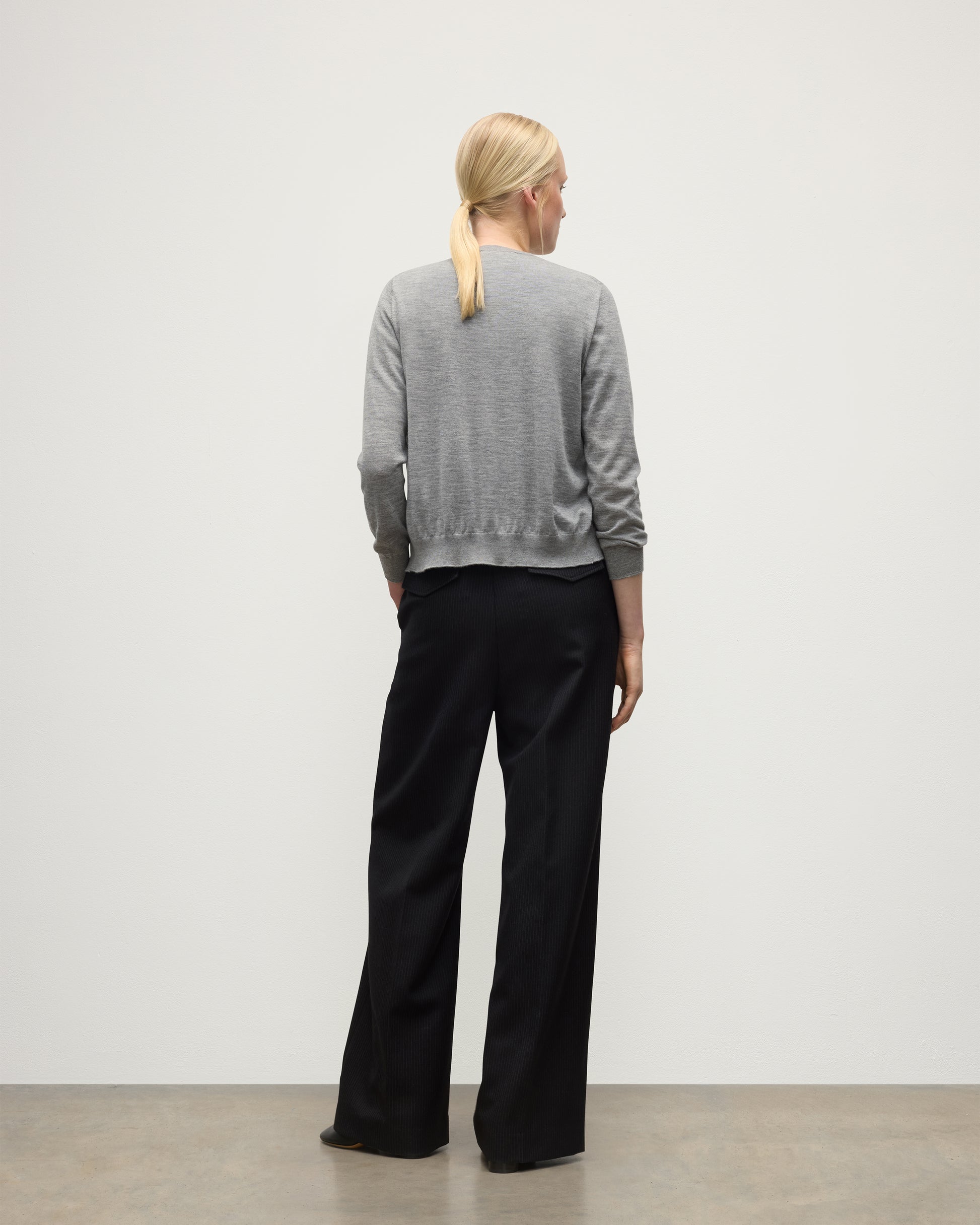 BACK OF A MODEL WEARING JOHNSTONS OF ELGIN WOMENS HONOR CREW CARDIGAN GREY 100% SUPERFINE CASHMERE OVER A MATCHING T-SHIRT WITH BLACK TROUSERS KAI05708HA4253