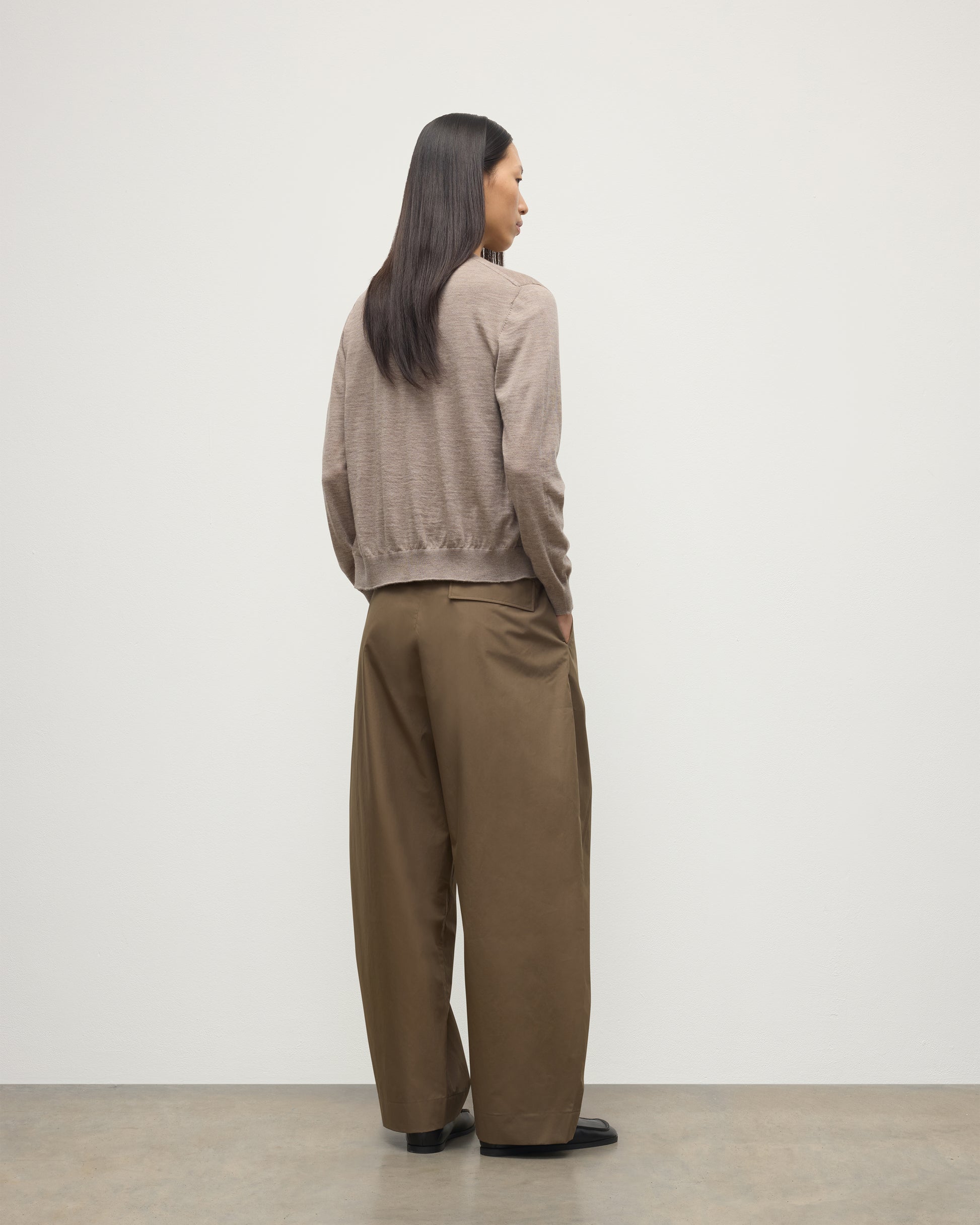 BACK OF MODEL WEARING JOHNSTONS OF ELGIN WOMENS HONOR CREW CARDIGAN LIGHT BROWN 100% SUPERFINE CASHMERE OVER A MATCHING CASHMERE T-SHIRT WITH BROWN WIDE LEG TROUSERS  KAI05708HB0273