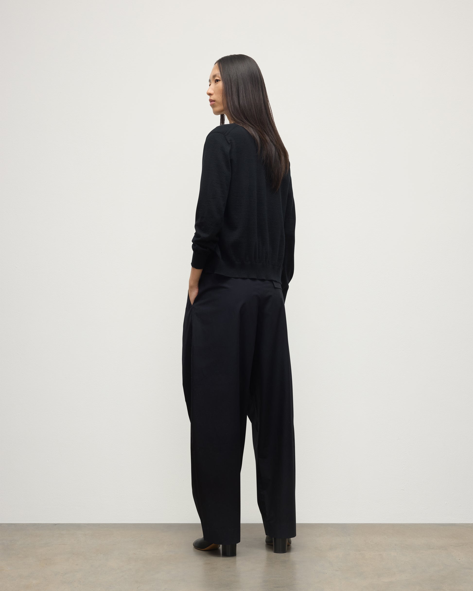 BACK OF MODEL WEARING JOHNSTONS OF ELGIN WOMENS HONOR CREW CARDIGAN BLACK 100% SUPERFINE CASHMERE OVER A MATCHING T-SHIRT AND NAVY WIDE LEG TROUSERS KAI05708SA7146