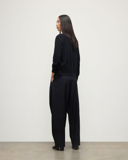 BACK OF MODEL WEARING JOHNSTONS OF ELGIN WOMENS HONOR CREW CARDIGAN BLACK 100% SUPERFINE CASHMERE OVER A MATCHING T-SHIRT AND NAVY WIDE LEG TROUSERS KAI05708SA7146
