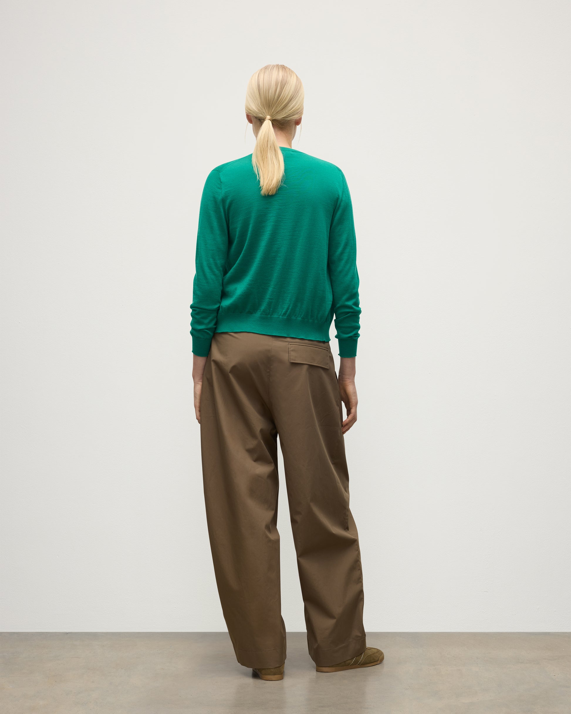 BACK OF MODEL WEARING JOHNSTONS OF ELGIN WOMENS HONOR CREW CARDIGAN GREEN 100% SUPERFINE CASHMERE WITH BROWN BELTED CHINOS KAI05708SC4714