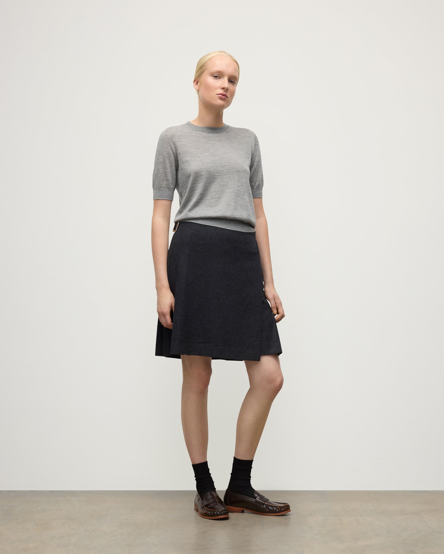 MODEL WEARS JOHNSTONS OF ELGIN WOMENS HONOR SHORT SLEEVE CREW GREY 100% SUPERFINE CASHMERE WITH SHORT LE KILT CHARCOAL KILT  KAI05712HA4253