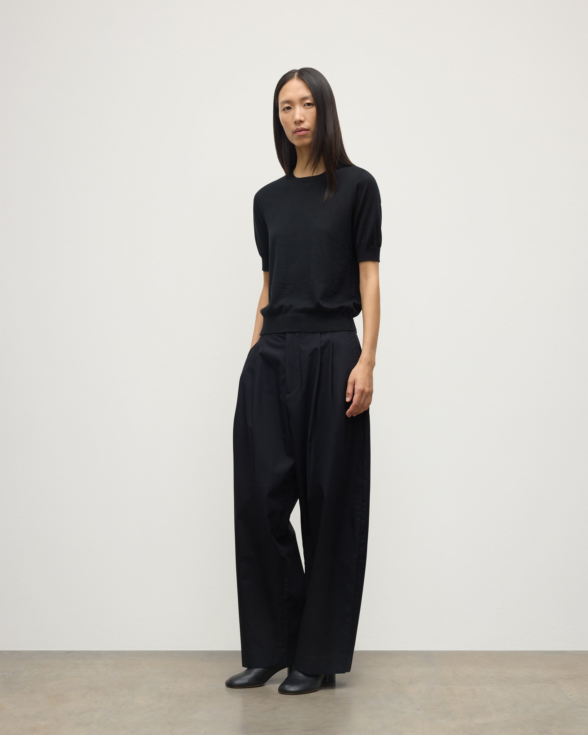 MODEL WEARS JOHNSTONS OF ELGIN WOMENS HONOR SHORT SLEEVE CREW BLACK 100% SUPERFINE CASHMERE WITH BLACK TROUSERS AND BOOTS KAI05712SA7146