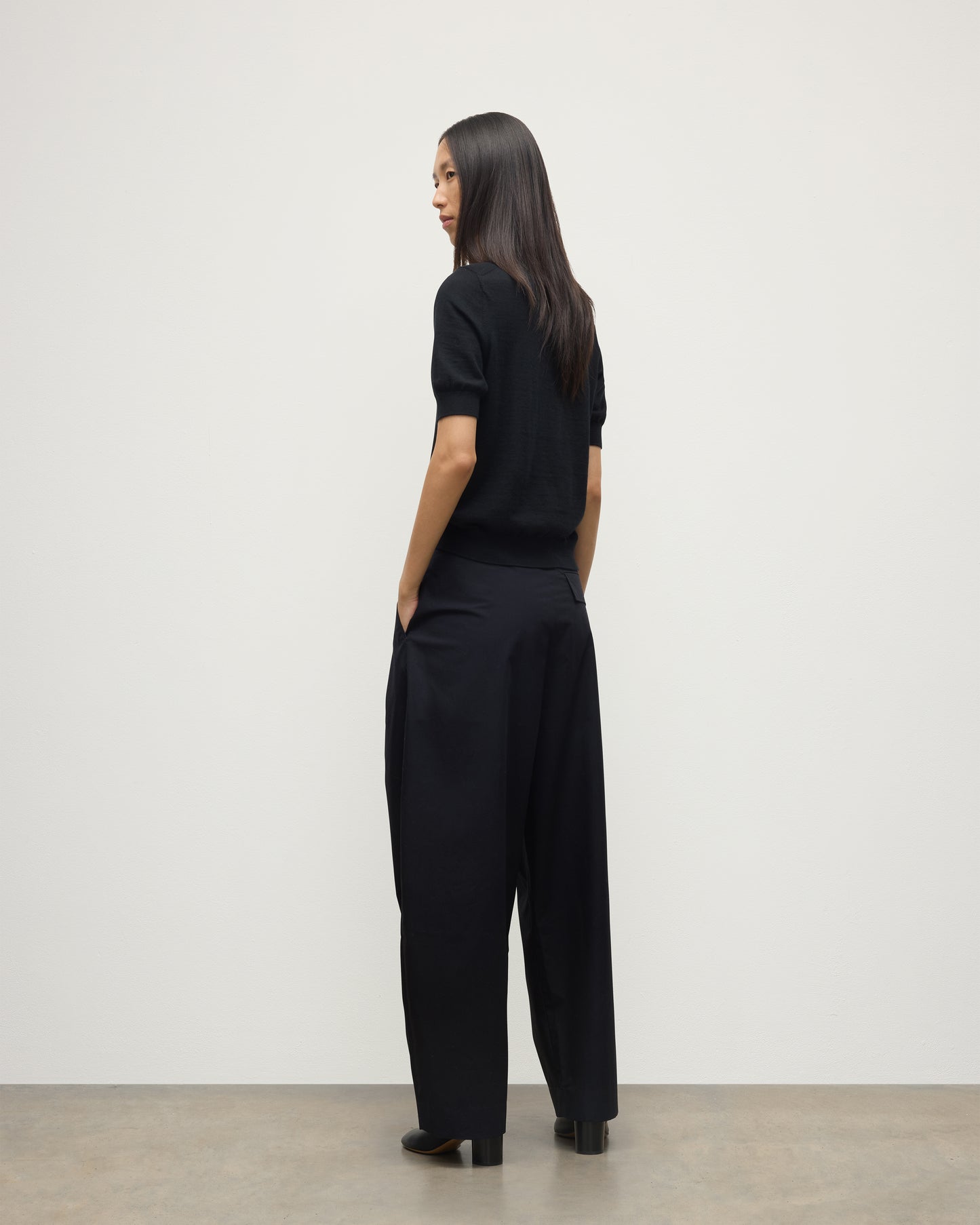 BACK OF A MODEL WEARS JOHNSTONS OF ELGIN WOMENS HONOR SHORT SLEEVE CREW BLACK 100% SUPERFINE CASHMERE WITH BLACK TROUSERS AND BOOTS KAI05712SA7146
