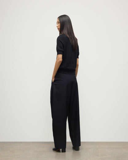 BACK OF A MODEL WEARS JOHNSTONS OF ELGIN WOMENS HONOR SHORT SLEEVE CREW BLACK 100% SUPERFINE CASHMERE WITH BLACK TROUSERS AND BOOTS KAI05712SA7146