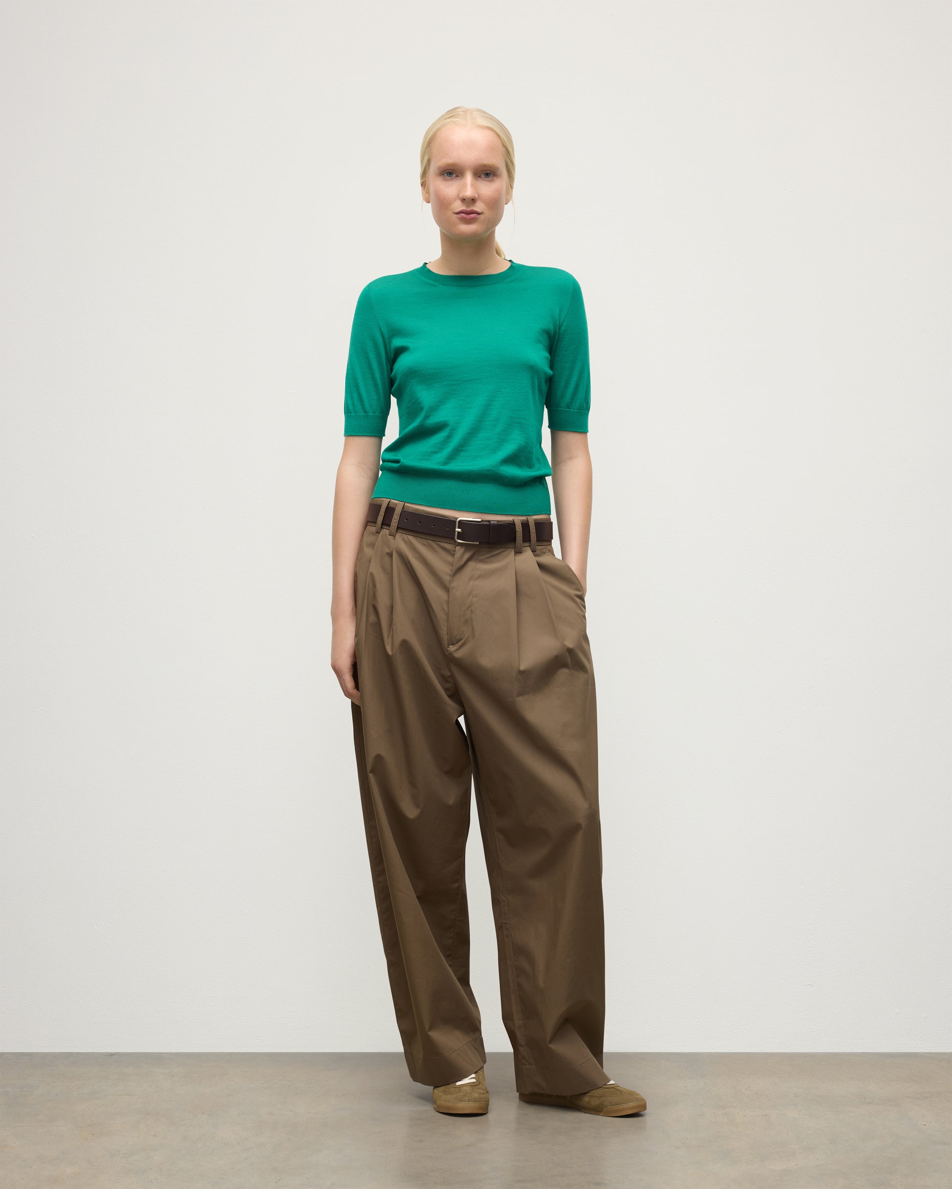 MODEL WEARS JOHNSTONS OF ELGIN WOMENS HONOR SHORT SLEEVE CREW GREEN 100% SUPERFINE CASHMERE WITH BROWN RELAXED TROUSERS AND TRAINERS KAI05712SC4714