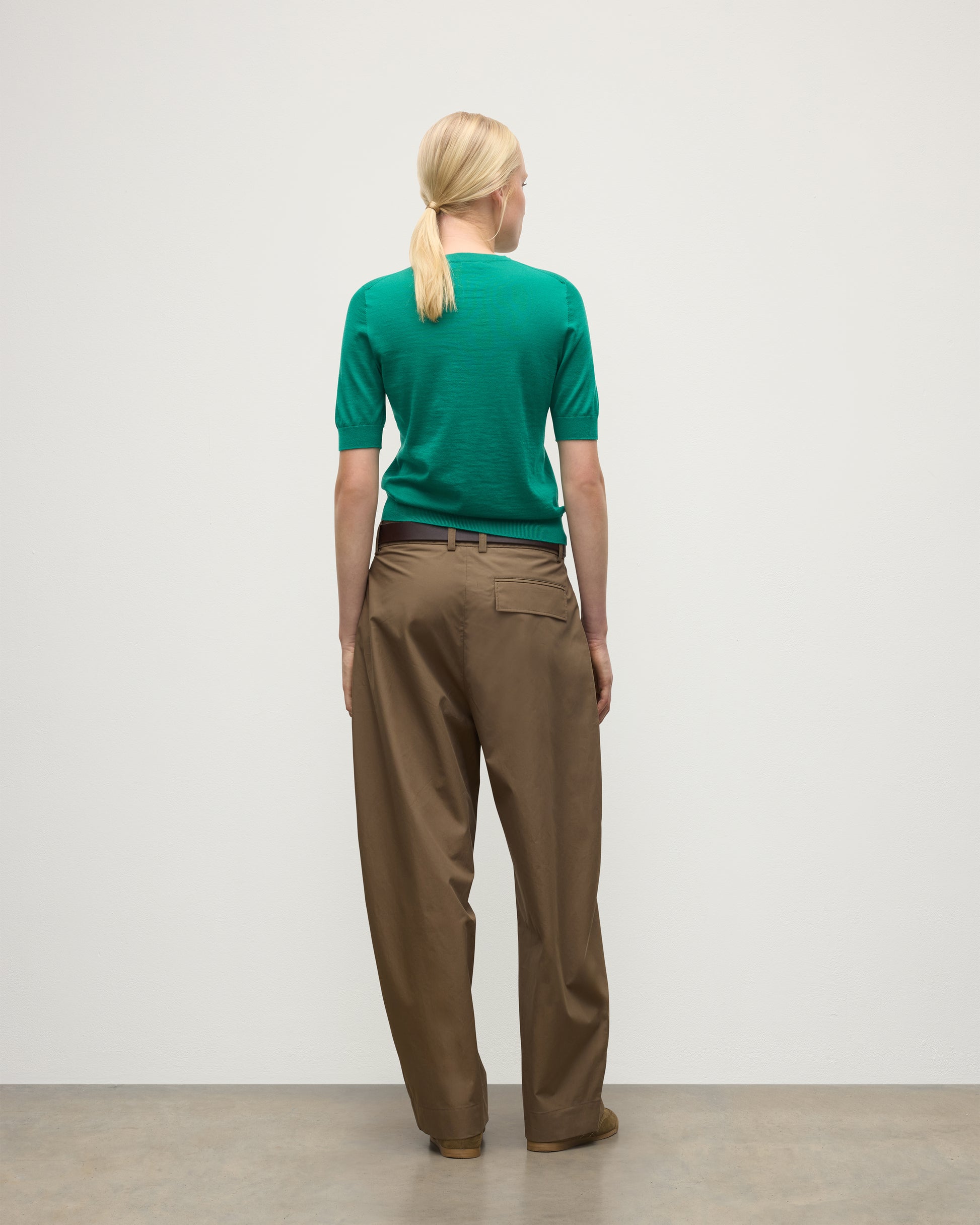 BACK OF MODEL WEARS JOHNSTONS OF ELGIN WOMENS HONOR SHORT SLEEVE CREW GREEN 100% SUPERFINE CASHMERE WITH BROWN RELAXED TROUSERS AND TRAINERS KAI05712SC4714