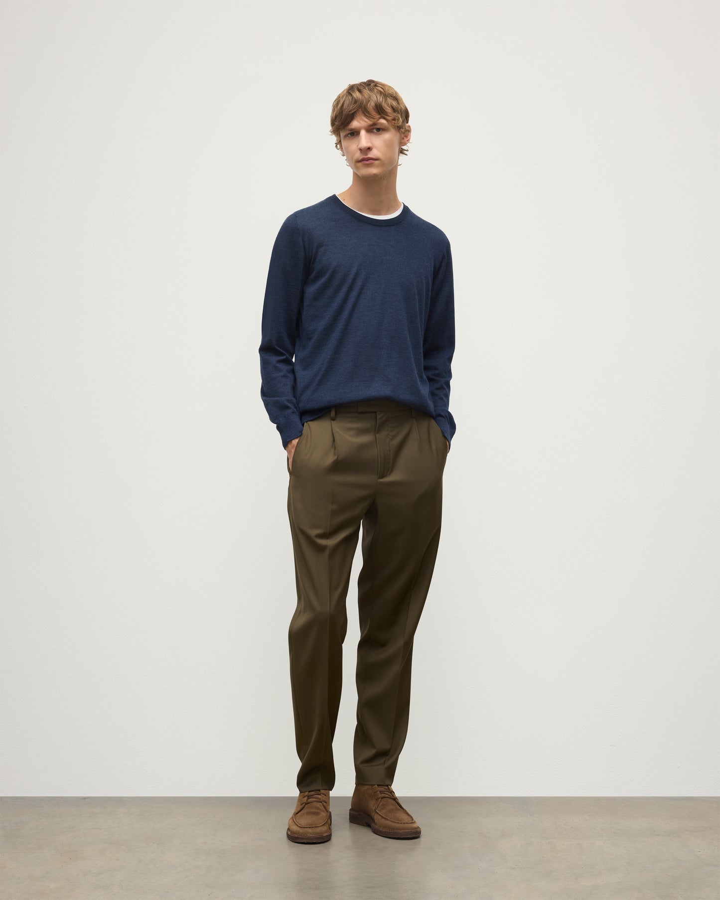 MODEL WEARING JOHNSTONS OF ELGIN MENS FIN SUPERFINE CREW NAVY 100% SUPERFINE CASHMERE OVER A WHITE T-SHIRT WITH OLIVE TROUSERS KAI05717HD7350