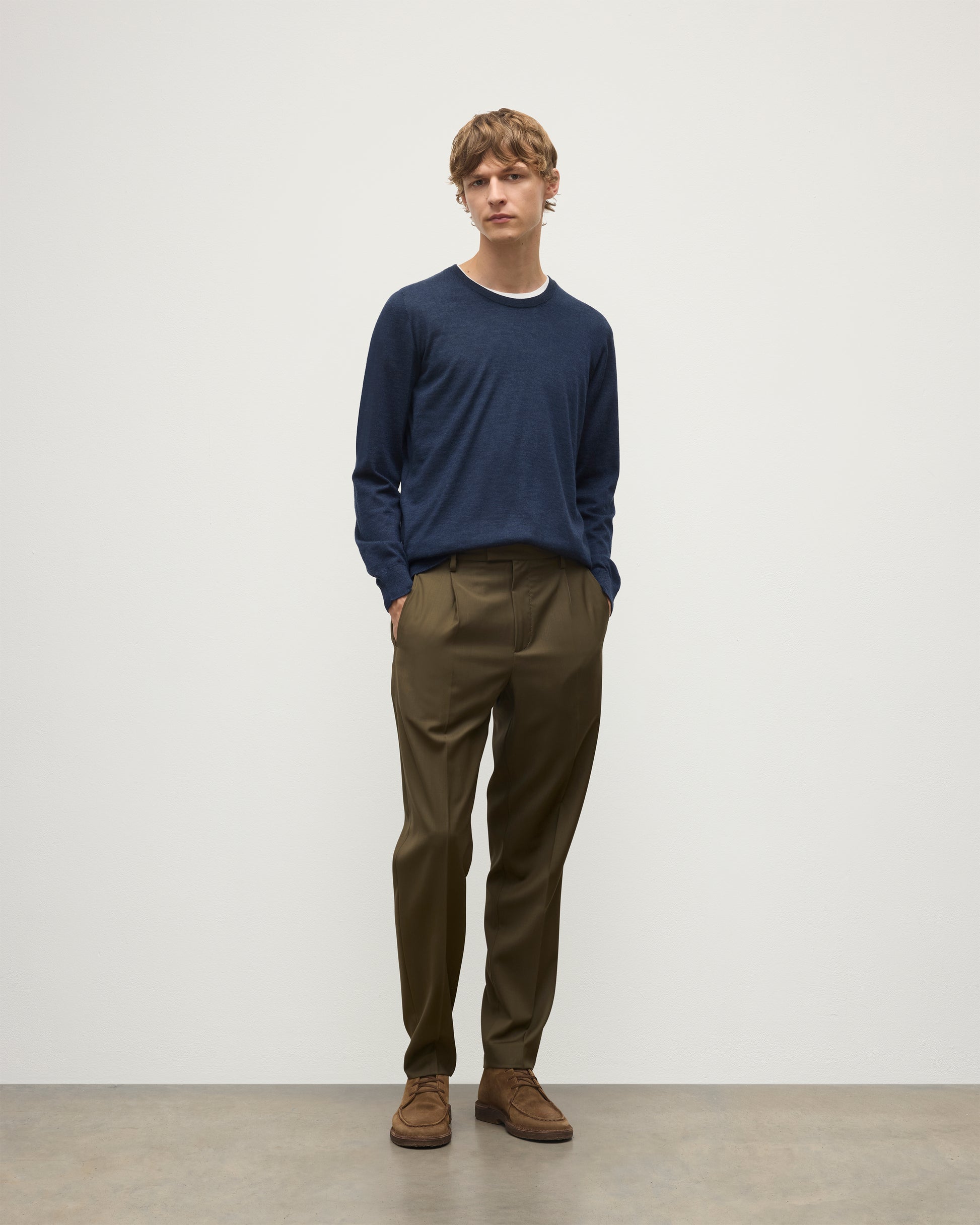 MODEL WEARING JOHNSTONS OF ELGIN MENS FIN SUPERFINE CREW NAVY 100% SUPERFINE CASHMERE OVER A WHITE T-SHIRT WITH OLIVE TROUSERS KAI05717HD7350