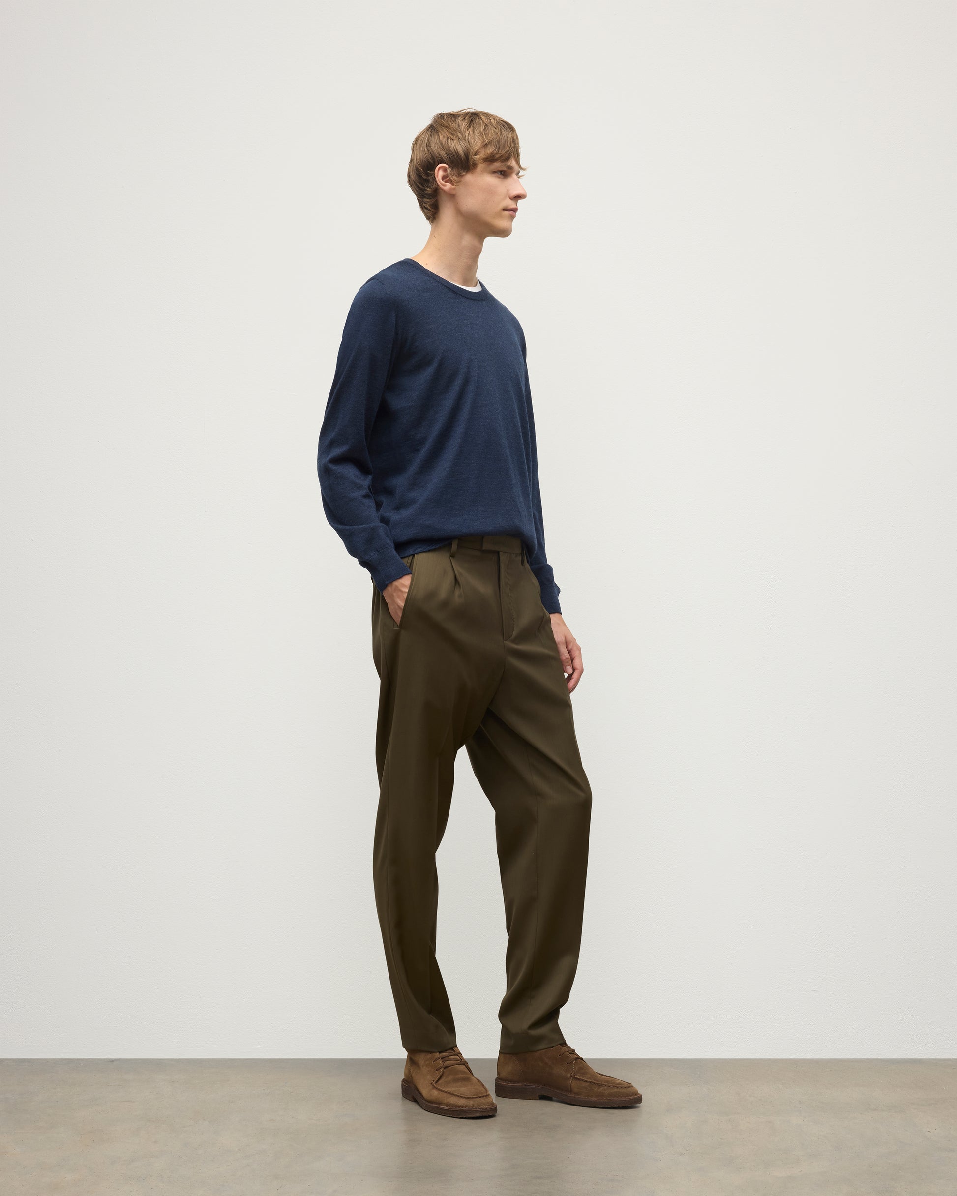 MODEL WEARING JOHNSTONS OF ELGIN MENS FIN SUPERFINE CREW NAVY 100% SUPERFINE CASHMERE OVER A WHITE T-SHIRT WITH OLIVE TROUSERS KAI05717HD7350