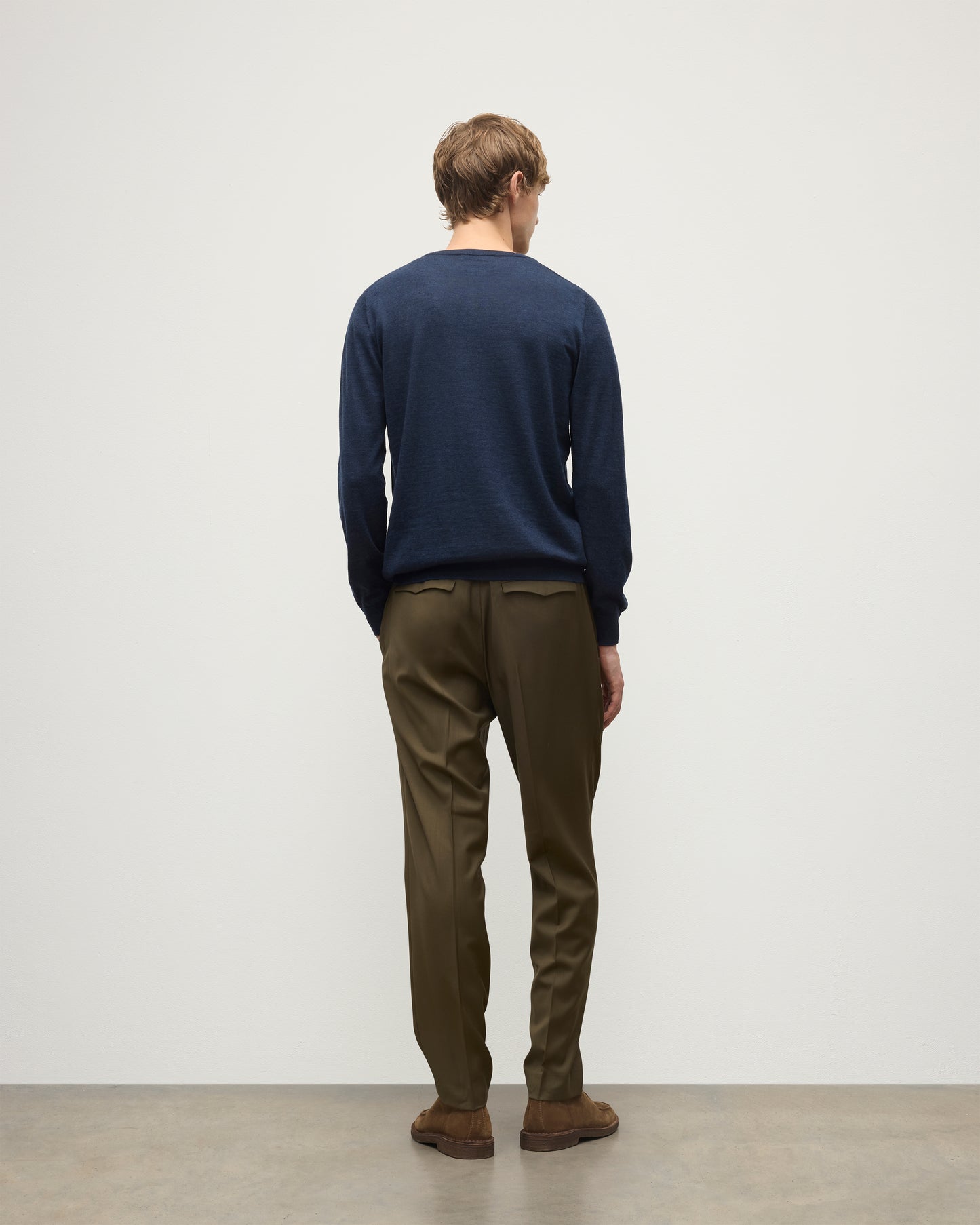 MODEL WEARING JOHNSTONS OF ELGIN MENS FIN SUPERFINE CREW NAVY 100% SUPERFINE CASHMERE OVER A WHITE T-SHIRT WITH OLIVE TROUSERS KAI05717HD7350
