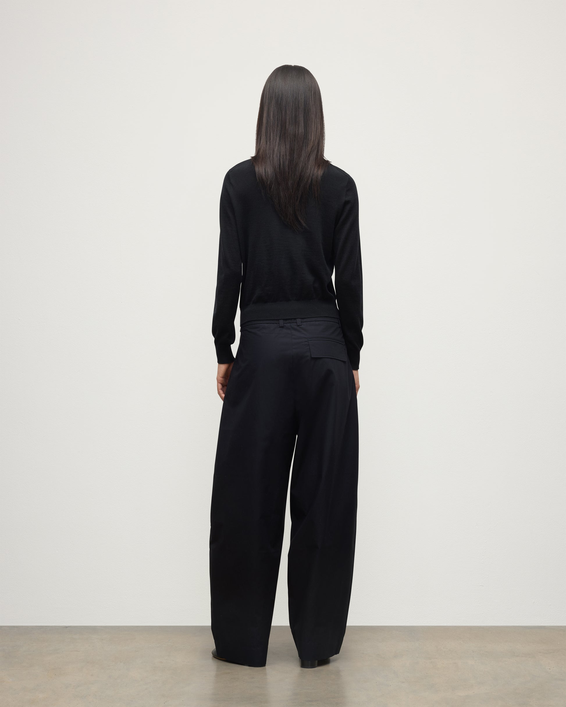 BACK VIEW OF MODEL WEARING JOHNSTONS OF ELGIN WOMENS ELLA SCOOP SWEATER BLACK WITH BLACK TROUSERS KAI05723SA7146