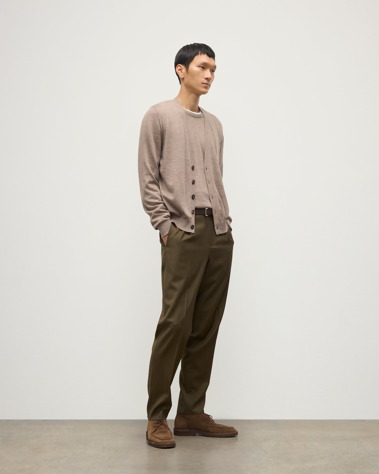 MALE MODEL WEARING JOHNSTONS OF ELGIN FORSYTH SUPERFINE VEE NECK CARDIGAN LIGHT BROWN  OVER A MATCHING SUPERFINE CASHMERE SWEATER AND OLIVE TROUSERS KAI05740HB0273