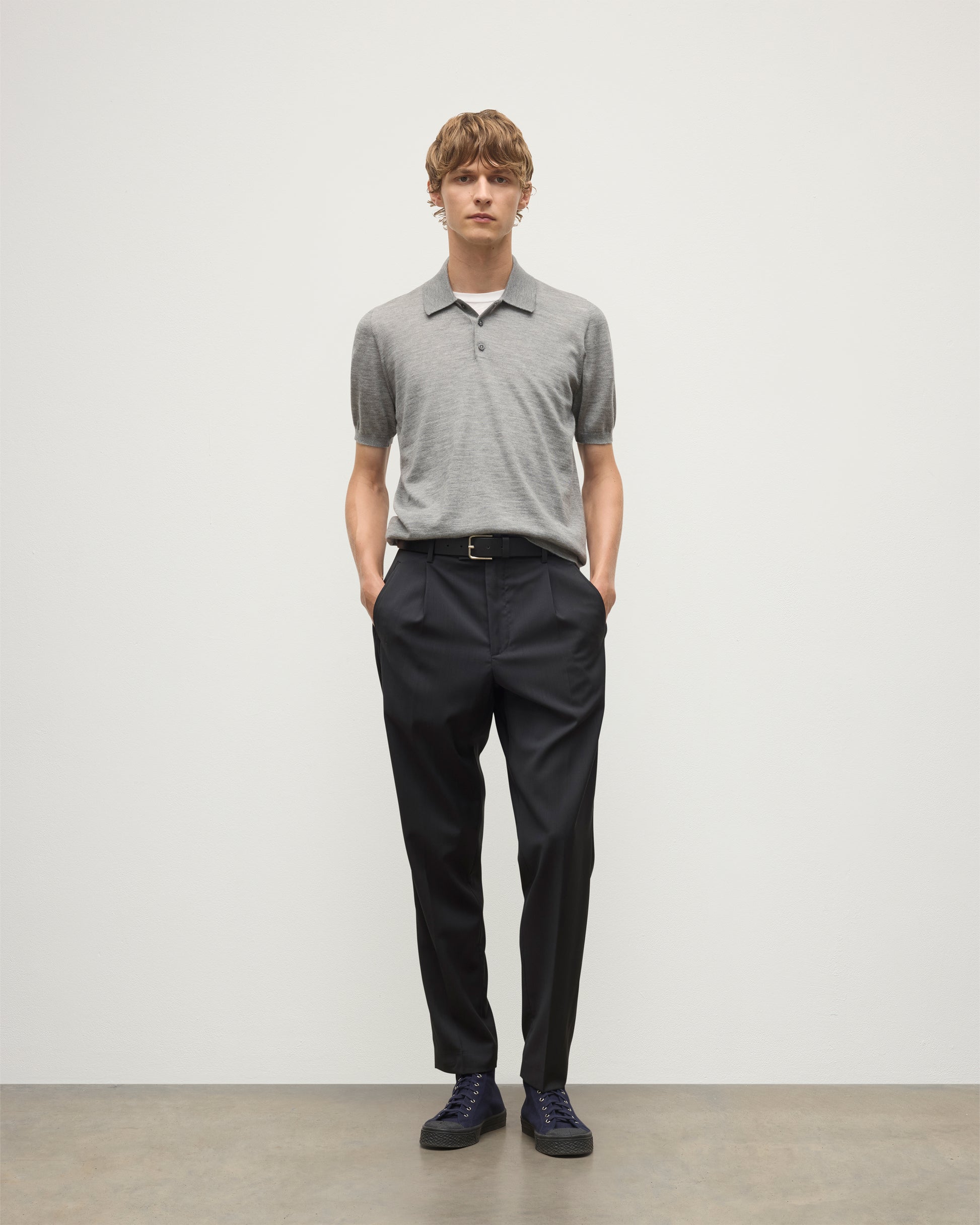 MODEL WEARS JOHNSTONS OF ELGIN MENS FIN SHORT SLEEVE SUPERFINE POLOSHIRT GREY OVER A WHITE T-SHIRT WITH NAVY TROUSERS KAI05741HA4253