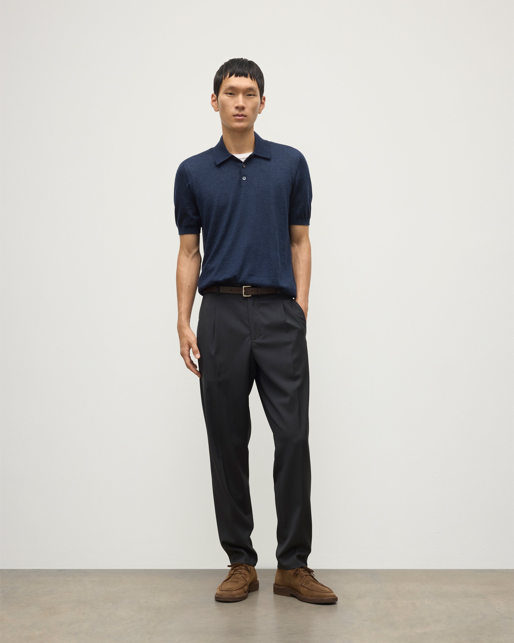 MODEL WEARS JOHNSTONS OF ELGIN MENS FIN SHORT SLEEVE SUPERFINE POLOSHIRT NAVY OVER A WHITE T-SHIRT WITH NAVY TROUSERS KAI05741HD7350