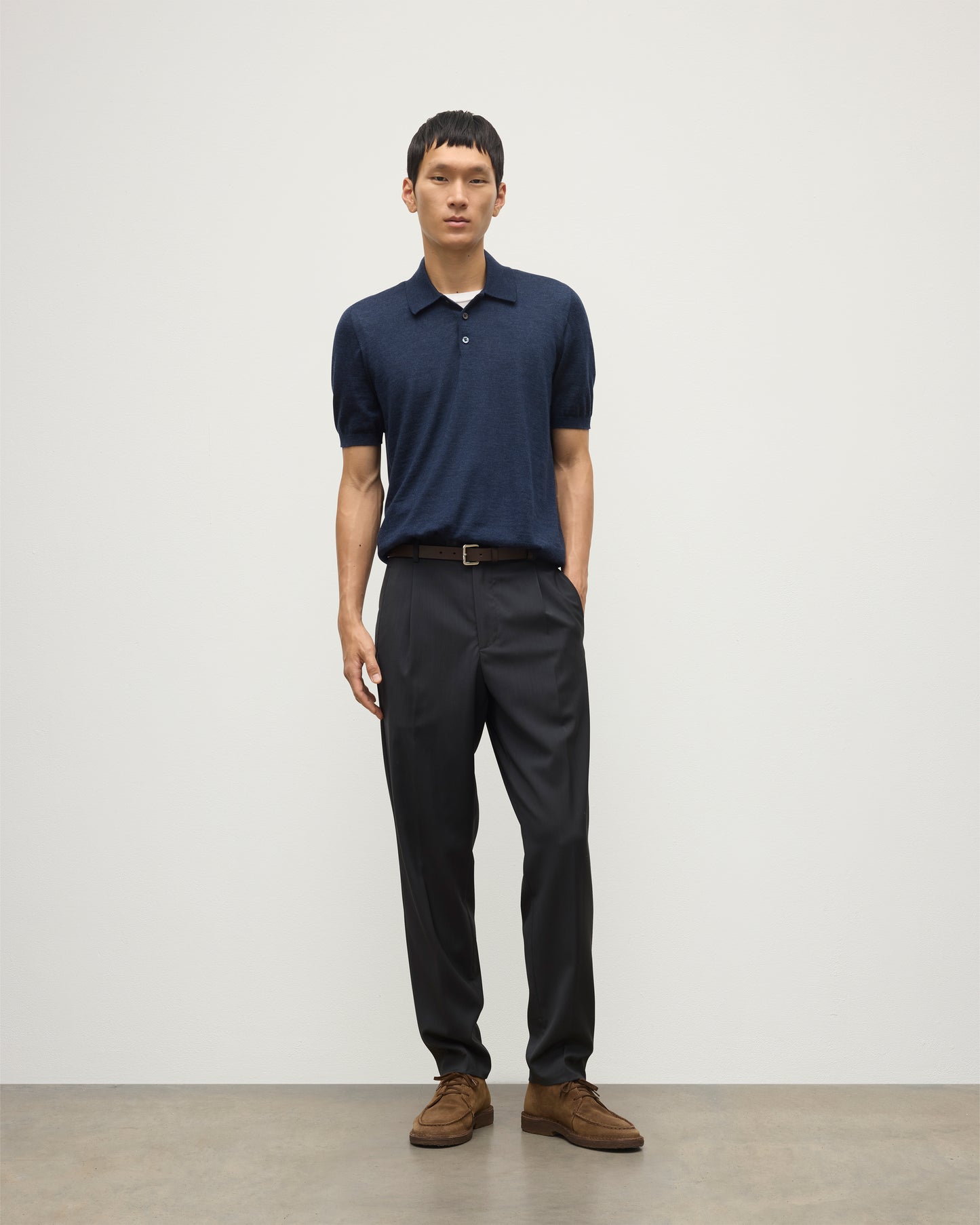 MODEL WEARS JOHNSTONS OF ELGIN MENS FIN SHORT SLEEVE SUPERFINE POLOSHIRT NAVY OVER A WHITE T-SHIRT WITH NAVY TROUSERS KAI05741HD7350