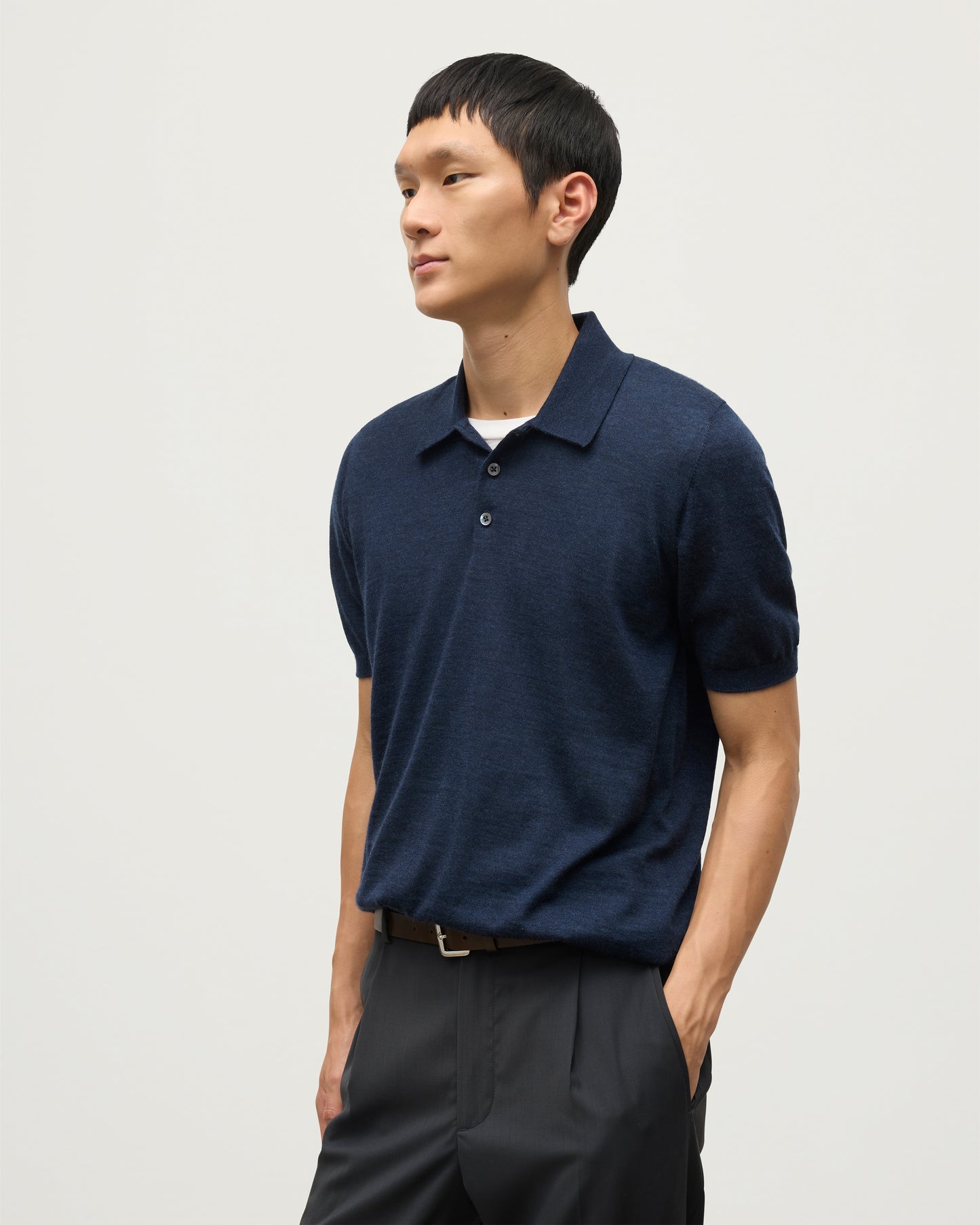 MODEL WEARS JOHNSTONS OF ELGIN MENS FIN SHORT SLEEVE SUPERFINE POLOSHIRT NAVY OVER A WHITE T-SHIRT WITH NAVY TROUSERS KAI05741HD7350