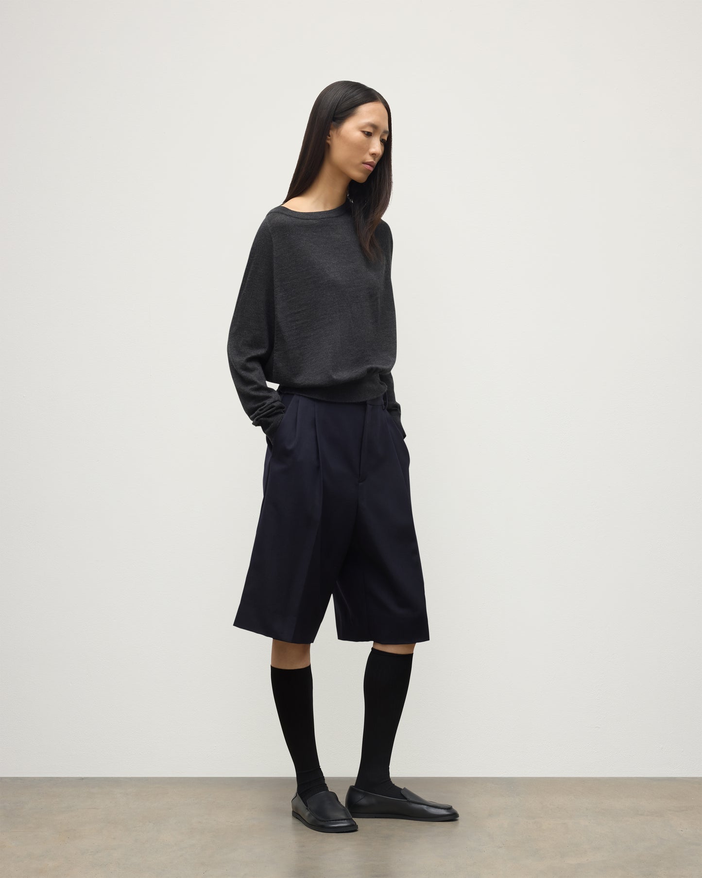 MODEL WEARING JOHNSTONS OF ELGIN WOMENS FINOLA SWEATER GREY 100% SUPERFINE CASHMERE  WITH BLACK LONG SHIRTS, SOCKS AND LOAFERS KAI05789HA7218