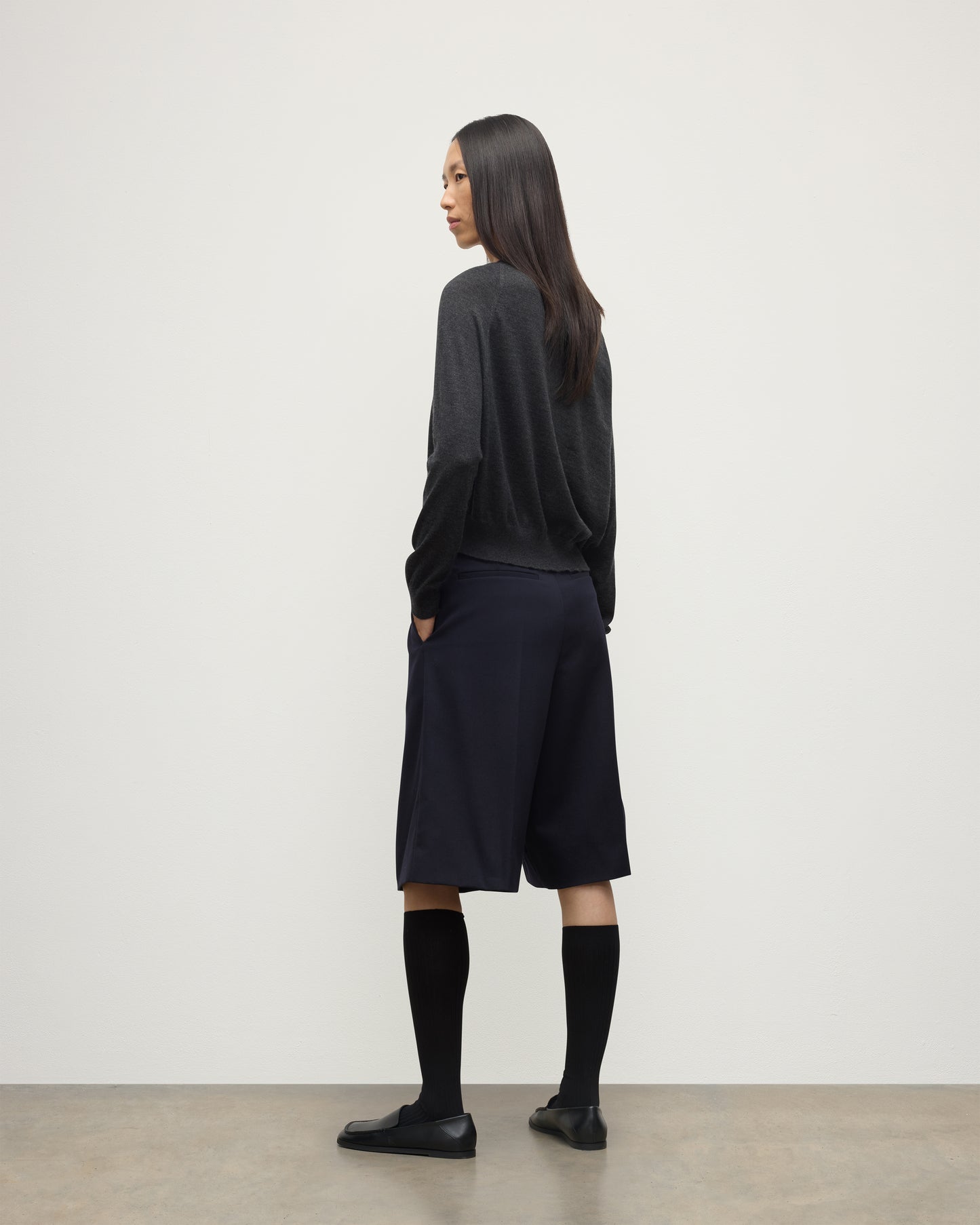 MODEL WEARING JOHNSTONS OF ELGIN WOMENS FINOLA SWEATER GREY 100% SUPERFINE CASHMERE  WITH BLACK LONG SHIRTS, SOCKS AND LOAFERS KAI05789HA7218