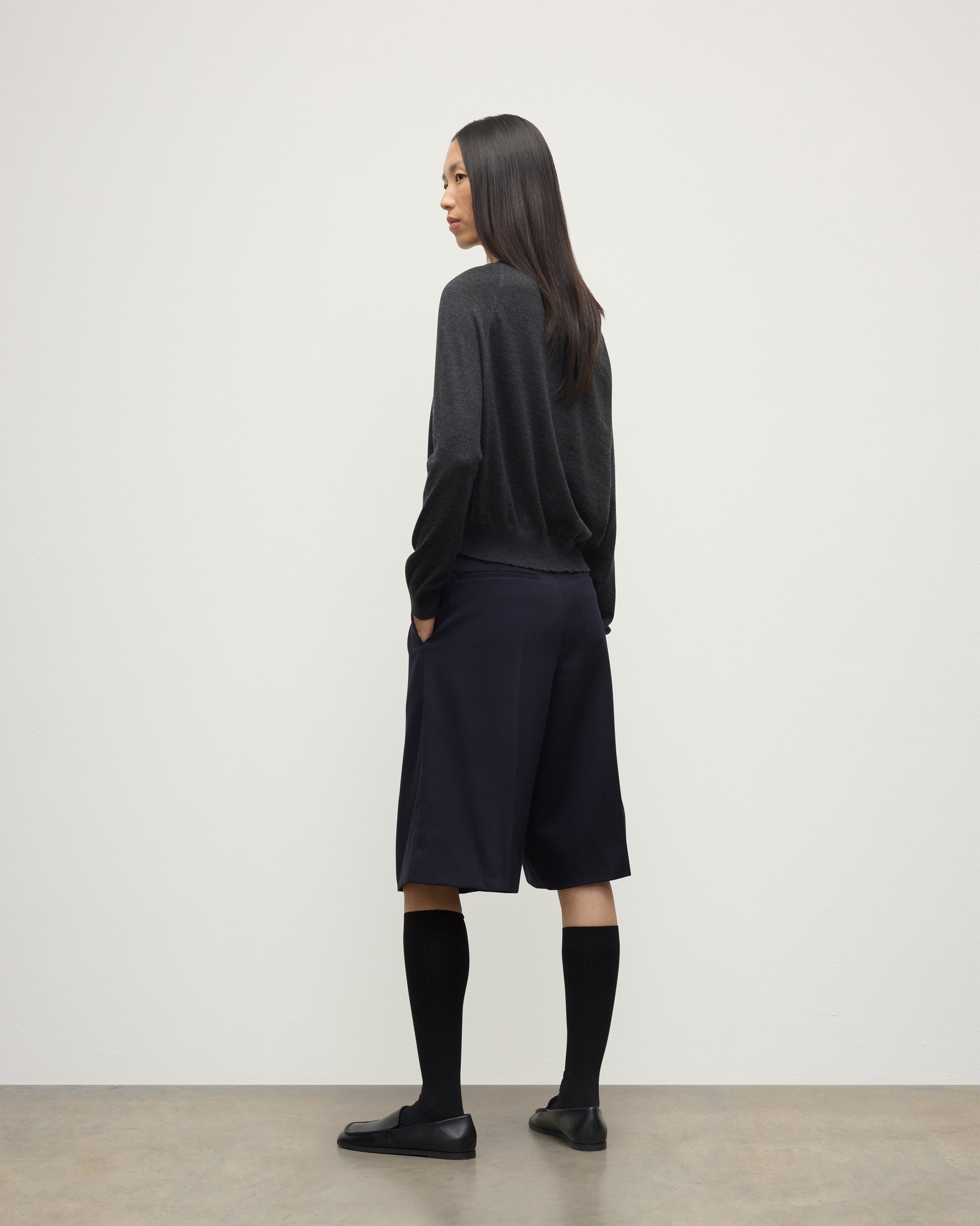 MODEL WEARING JOHNSTONS OF ELGIN WOMENS FINOLA SWEATER GREY 100% SUPERFINE CASHMERE  WITH BLACK LONG SHIRTS, SOCKS AND LOAFERS KAI05789HA7218