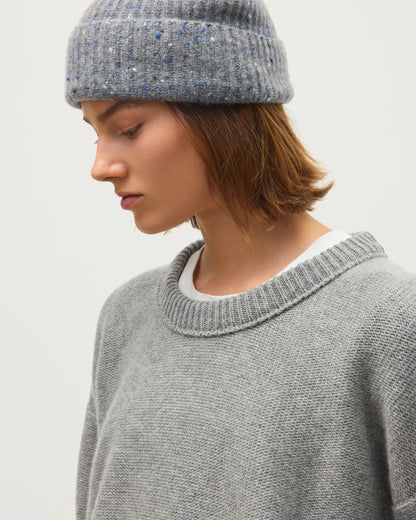 A close-up of a person wearing a gray knit crewneck sweater and a speckled gray beanie against a plain light background. JOHNSTONS OF ELGIN MAGGIE CREW SWEATER CASHMERE REVERSE STITCH ROUND NECK SWEATER - 8 PLY GREY 100% CASHMERE KAI05990HA0400