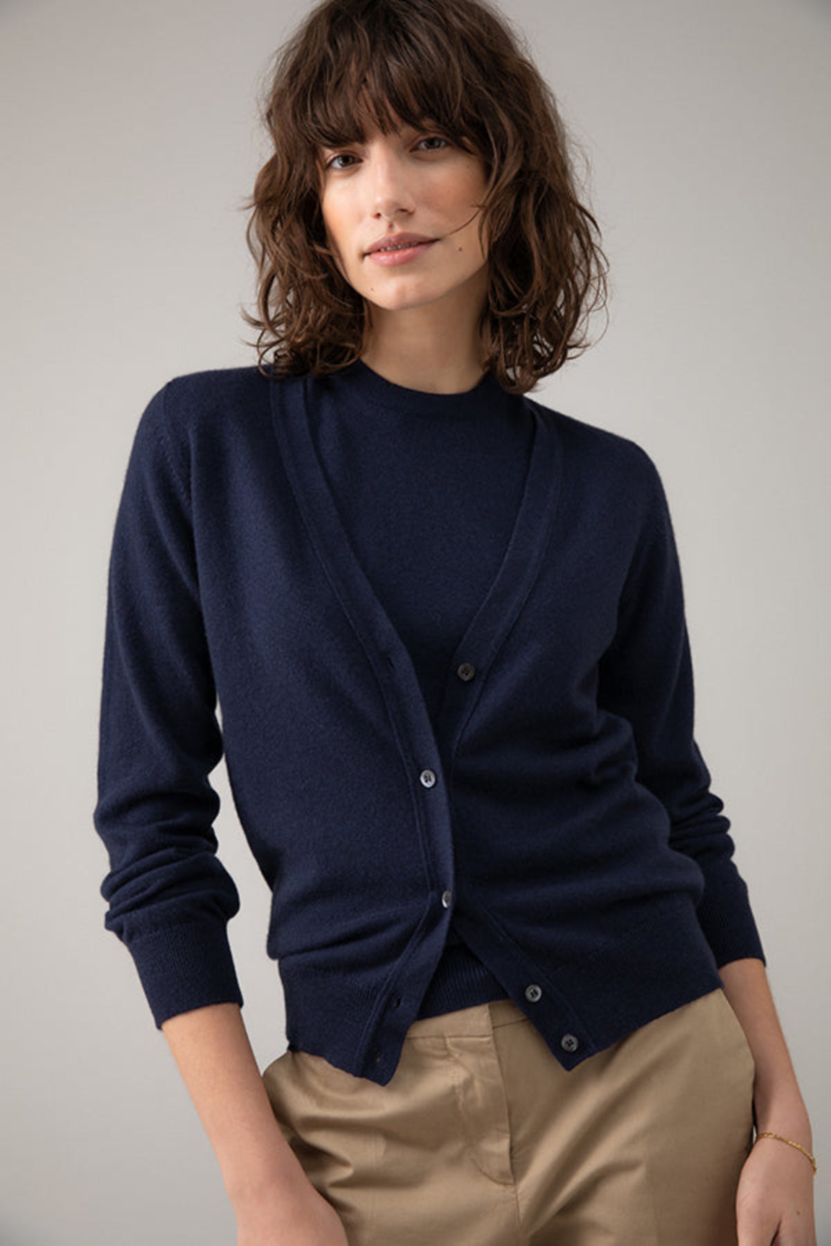 Woman wearing a navy cardigan over a black top with beige pants on a plain background KAP04508SD7286
