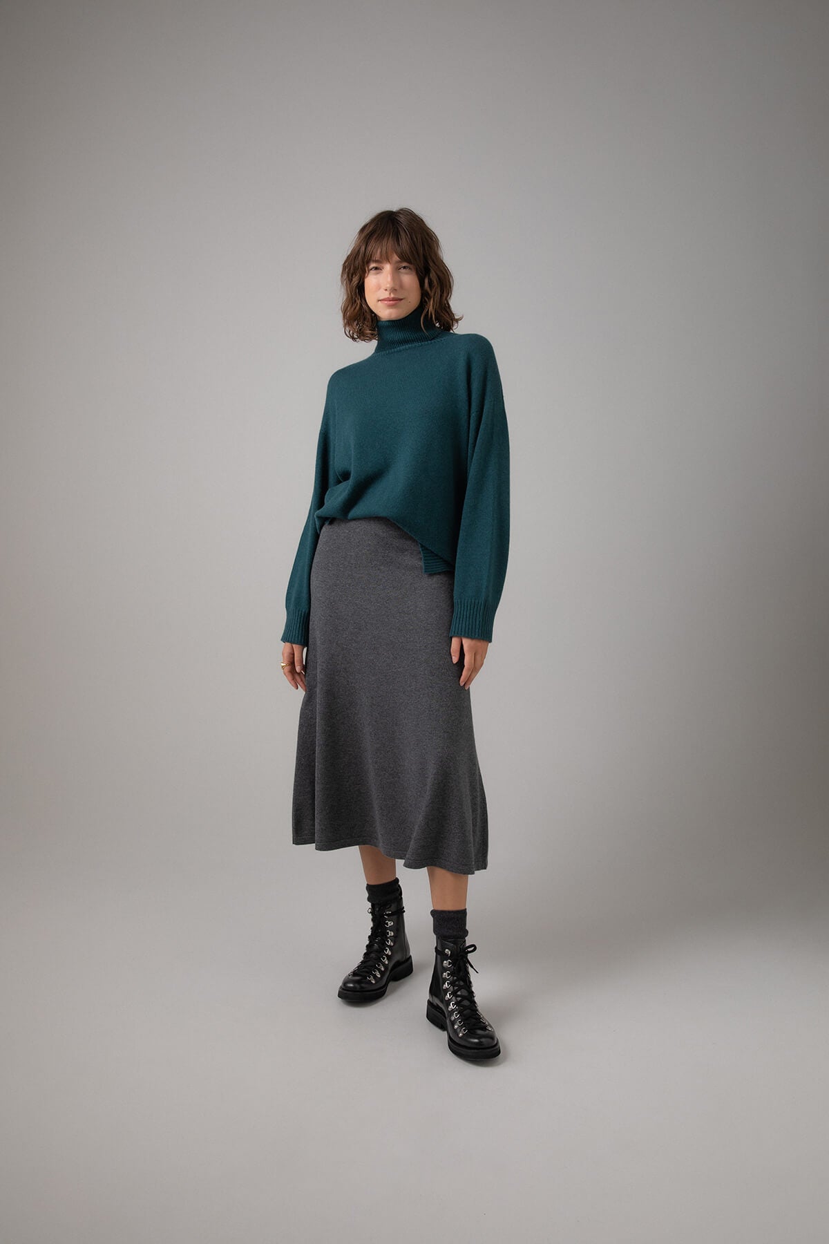 Johnstons of Elgin Women's A-Line Cashmere Skirt in Mid Grey worn with a Mallard Roll Neck Sweater on a grey background KAP05097HA4181