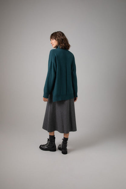 Back view of a Johnstons of Elgin Women's A-Line Cashmere Skirt in Mid Grey worn with a Mallard Roll Neck Sweater on a grey background KAP05097HA4181