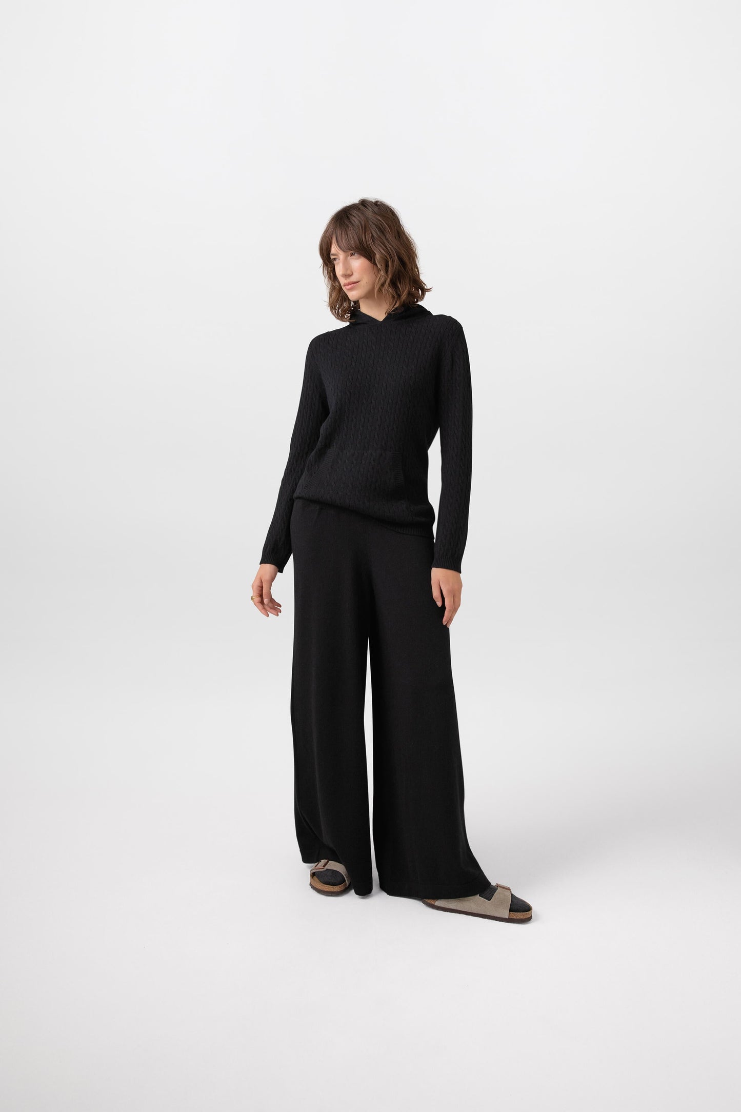 Johnstons of Elgin Women's Cashmere Slouch Pants in Black worn with a matching Cable Hoodie on a grey background KBP00924SA7099