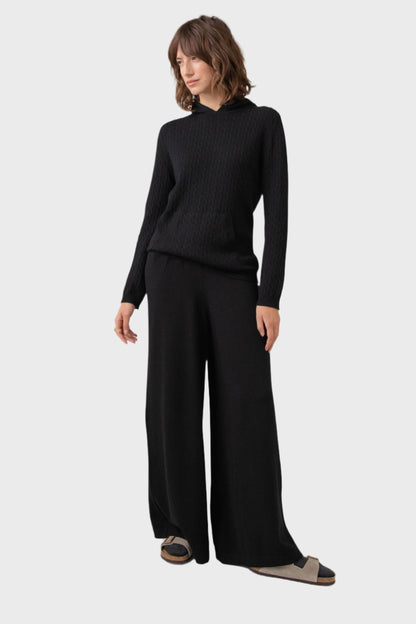 Johnstons of Elgin Women's Cashmere Slouch Pants in Black worn with a matching Cable Hoodie on a grey background KBP00924SA7099