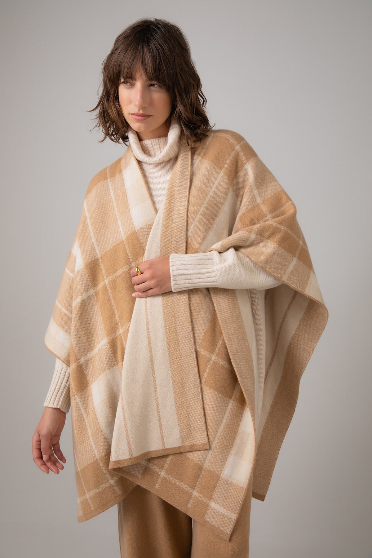 Details of a Johnstons of Elgin Double Face Cashmere Check Cape in Camel Check worn with Cream Cashmere Roll Neck and Camel Culottes on a grey background KAP05104JU1548ONE