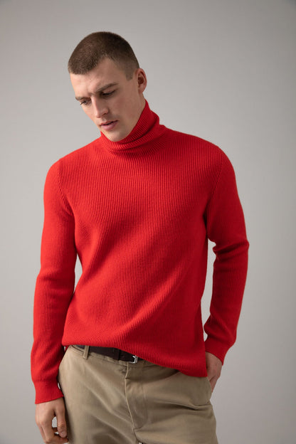 Johnstons of Elgin Men’s Ribbed Cashmere Roll Neck Jumper in Orkney Red on model wearing camel trousers on grey background KAP05107SE0661