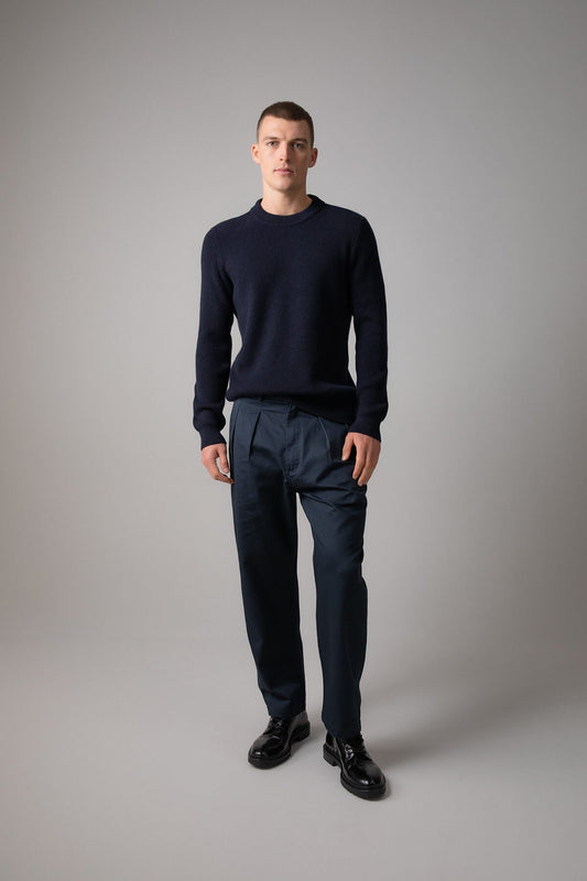Johnstons of Elgin Men’s Ribbed Cashmere Round Neck Jumper in Dark Navy on model wearing navy trousers on grey background KAP05144SD7286