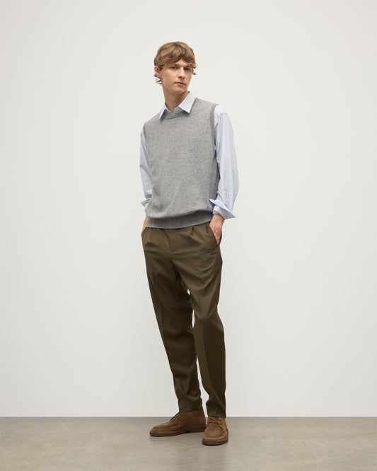 MODEL WEARS JOHNSTONS OF ELGIN MENS LENNOX SLEEVELESS CREW GREY 100% CASHMERE OVER A LIGHT BLUE SHIRT WITH OLIVE GREEN TROUSERS KAP05243HA0400