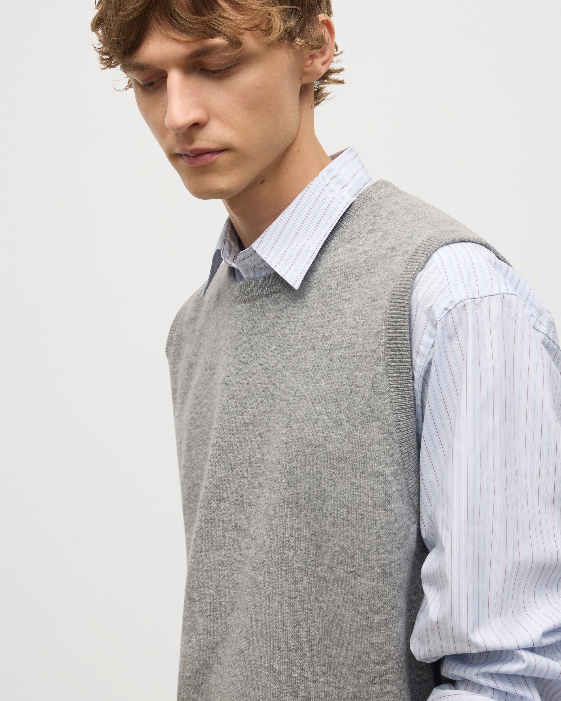 MODEL WEARS JOHNSTONS OF ELGIN MENS LENNOX SLEEVELESS CREW GREY 100% CASHMERE OVER A LIGHT BLUE SHIRT KAP05243HA0400